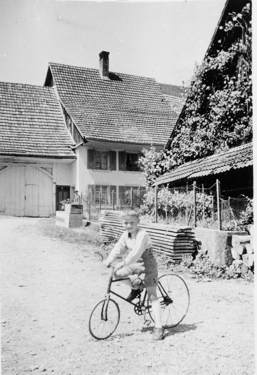 Um 1950 - Hermann Schweizer auf Fahrrad mit Eisenrädern. Bachoferhaus von hinten (heutige ehemalige Metzgerei Koster, Schupaferterstrasse 5).